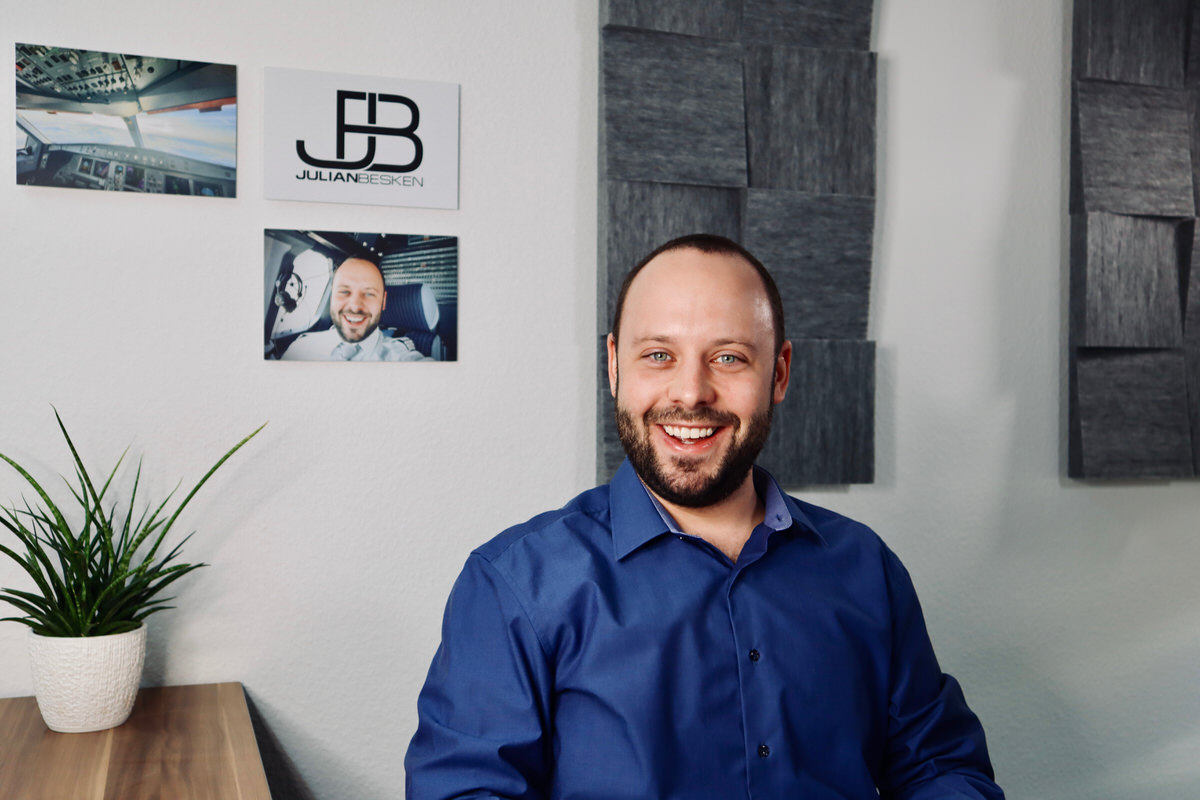 Julian Besken im Büro, im Hintergrund Cockpit-Aufnahmen und das Firmenlogo